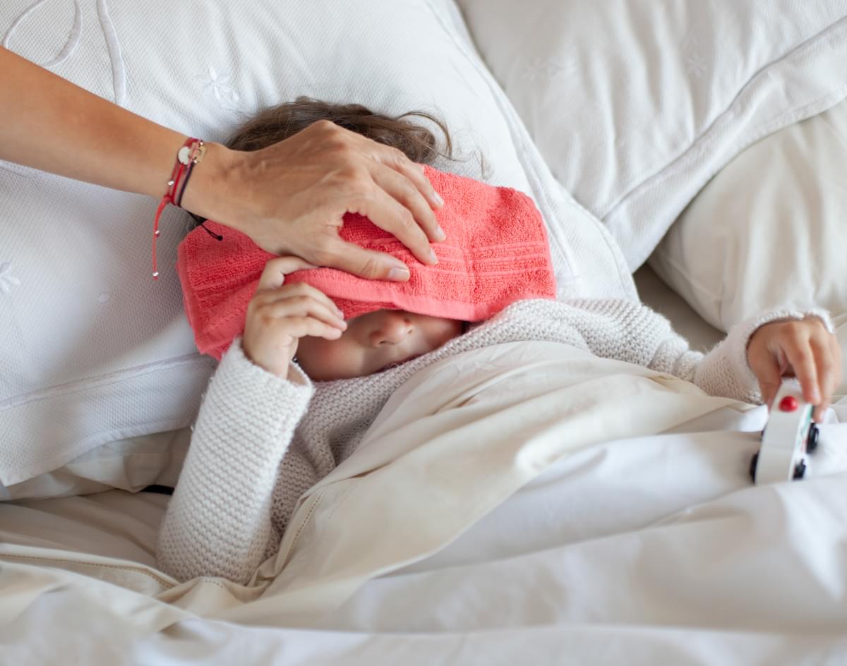 Niña enferma en cama, su madre le pone un paño húmedo en su cabeza para ayudar a bajarle la fiebre
